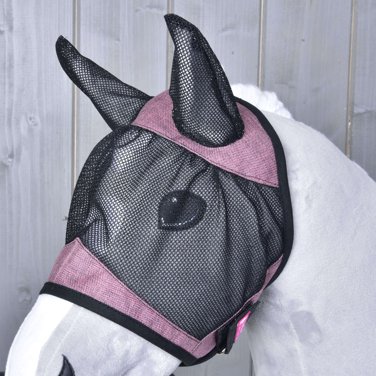 Gros plan de côté sur le masque anti-mouches d’un Hobby Horse gris, filet noir sur l’œil et bandes roses bordées de noir