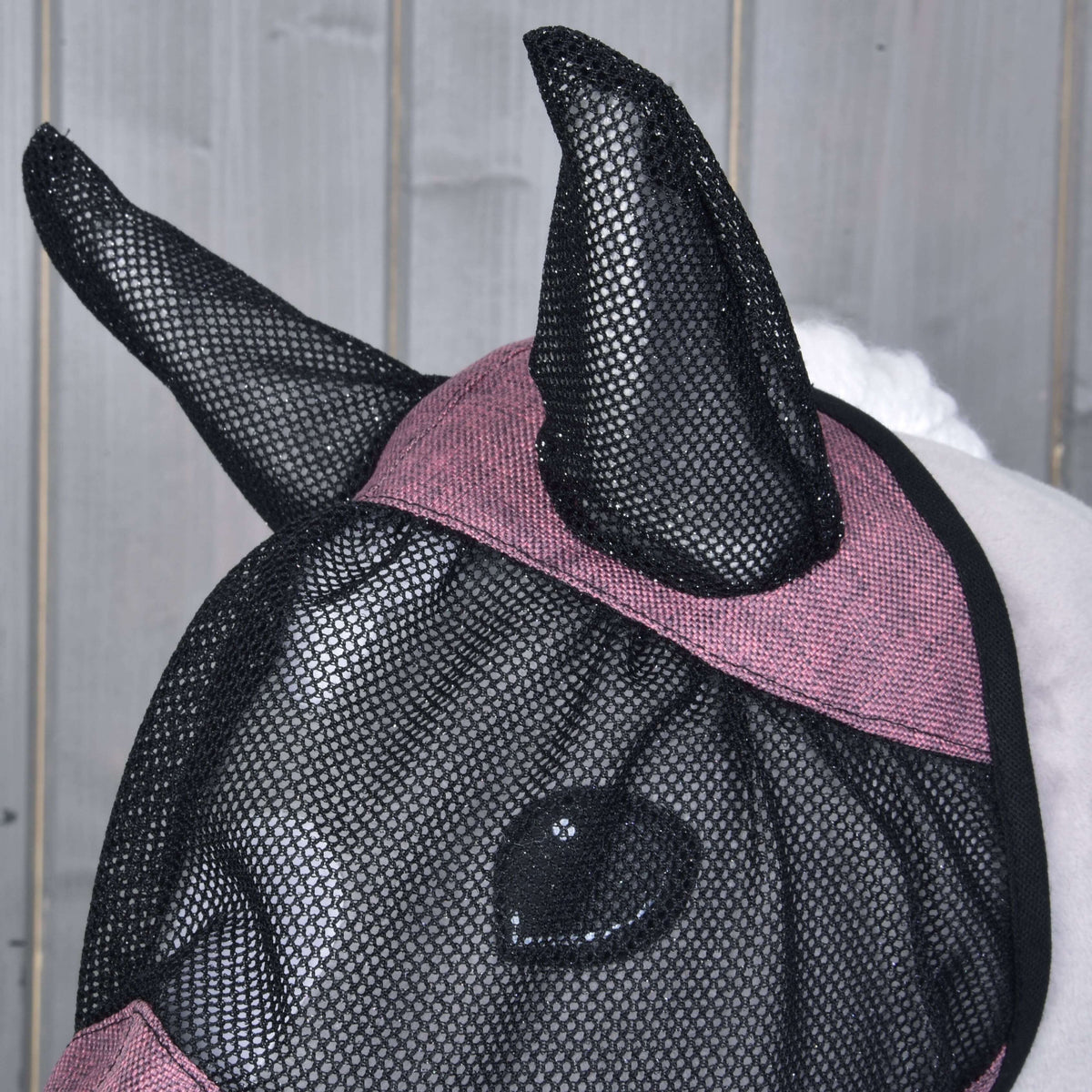 Gros plan sur les oreilles en filet noir et la bande rose chinée sur le front du masque anti-mouches