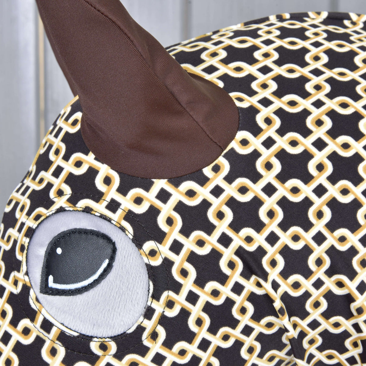 Close-up of the Luxus Design protective suit: brown fabric ear and a grey appliqué eye on the brown and cream geometric print