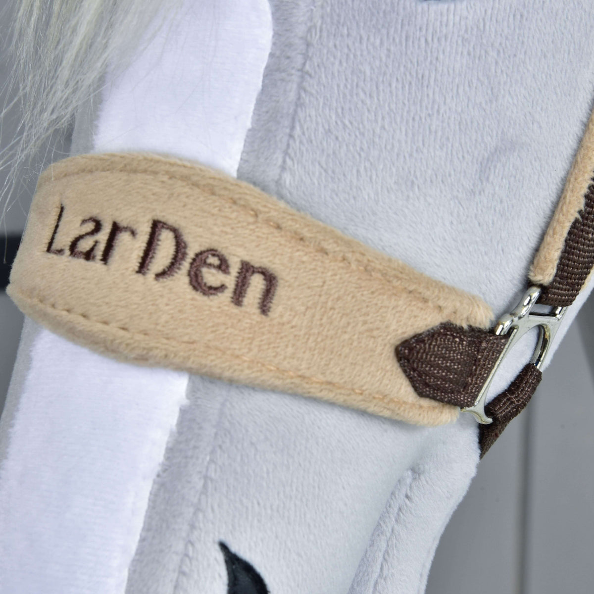 Close-up van de beige fleece neusriem met LarDen in donkerbruin garen geborduurd, naast een witte bles