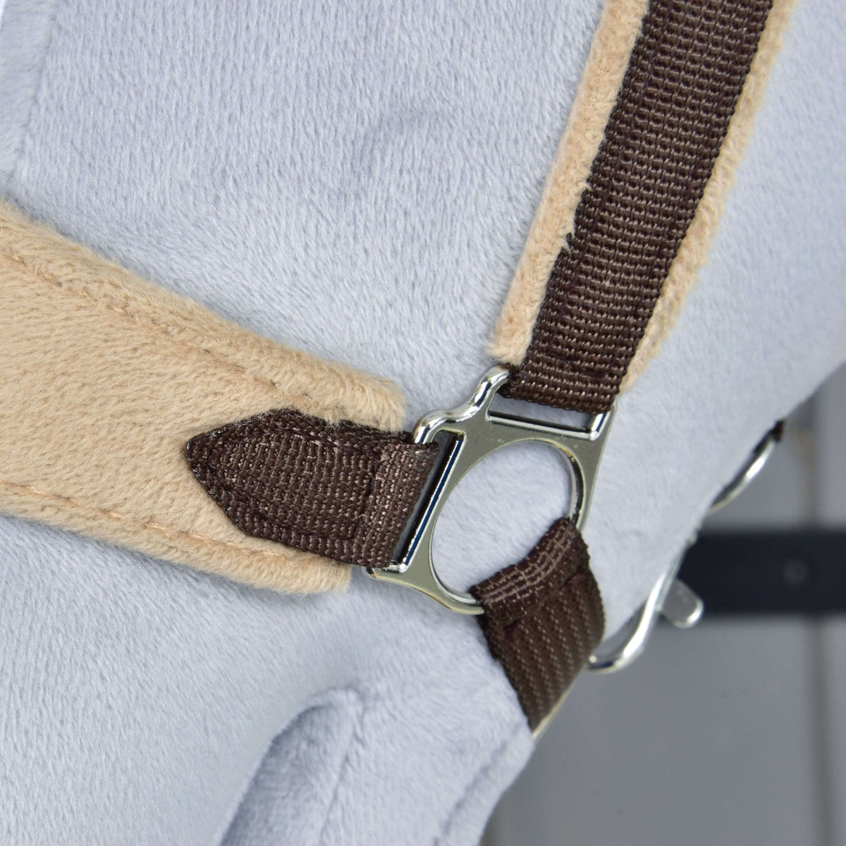 Close-up van de zilveren zijring die de donkerbruine wangriem verbindt met de beige fleece neusriem van de bruine halster met bont