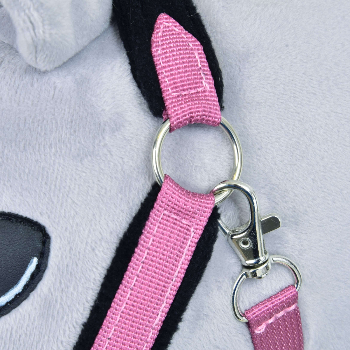 Close-up of the pink fur halter's cheek strap with black fur lining, a silver ring and a snap hook on light grey plush