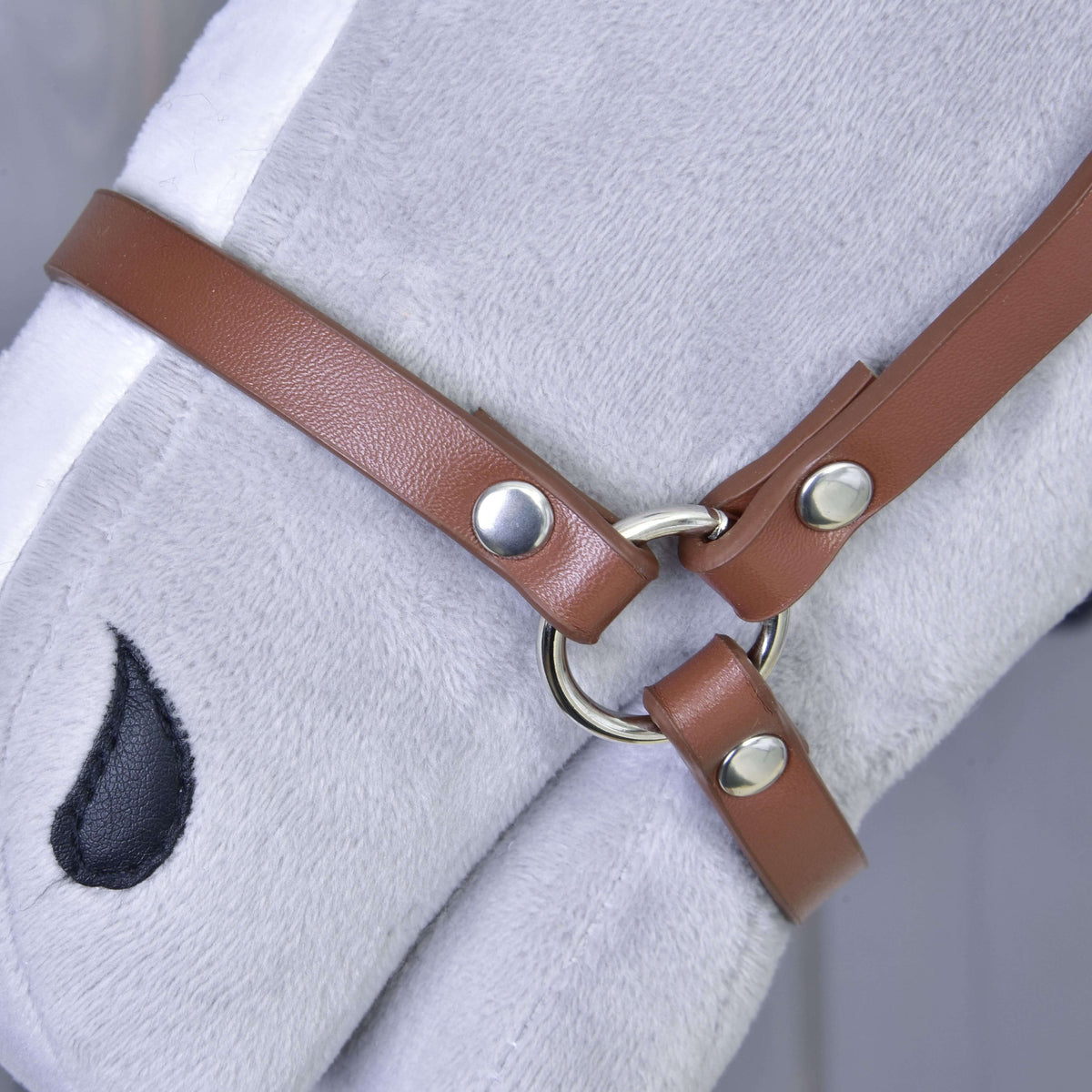 Close-up of the brown leatherette halter with a silver ring and rivets on the noseband of a grey plush Hobby Horse