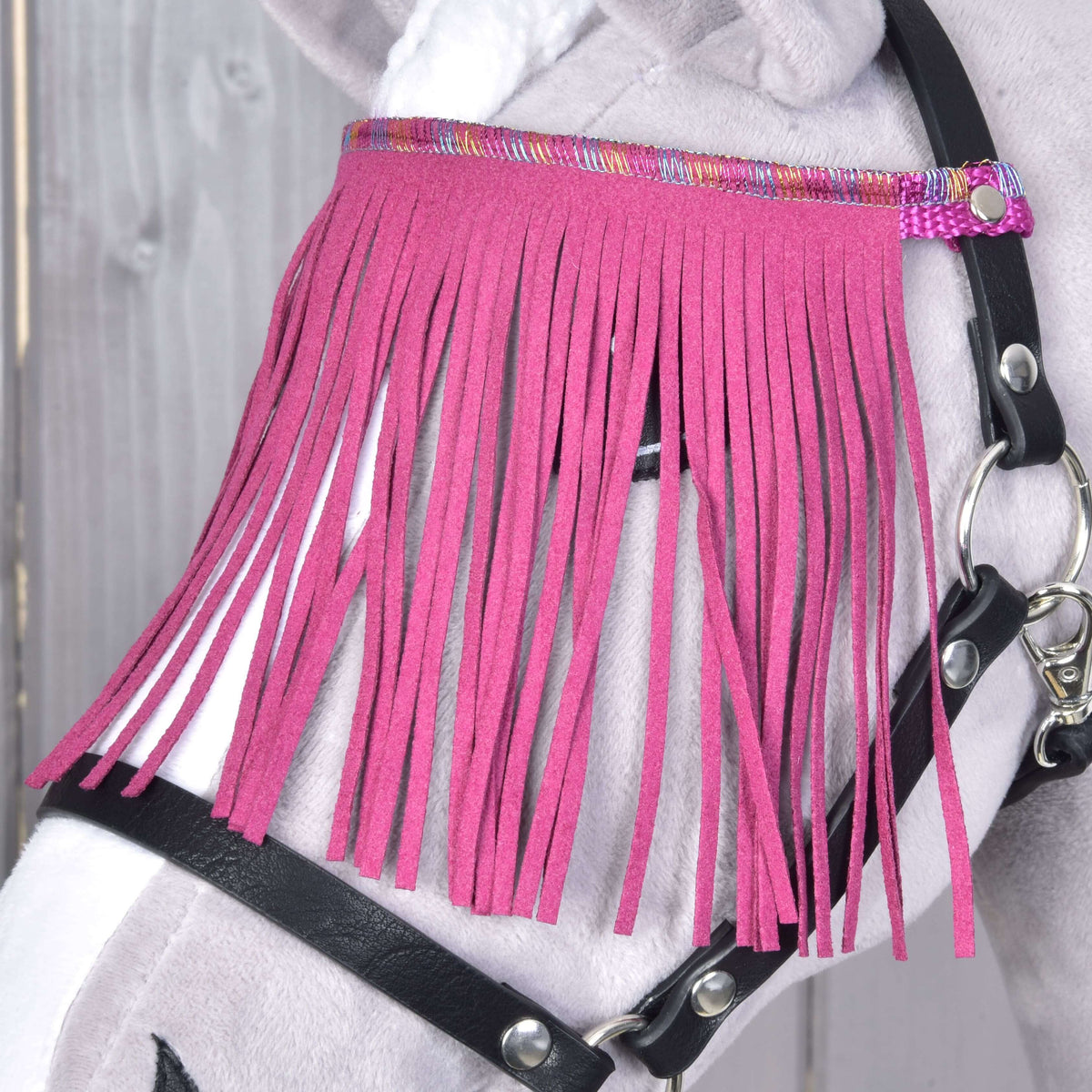 Close-up of the pink fringe covering the eye of a grey Hobby Horse, hung from a shimmering band on the black halter