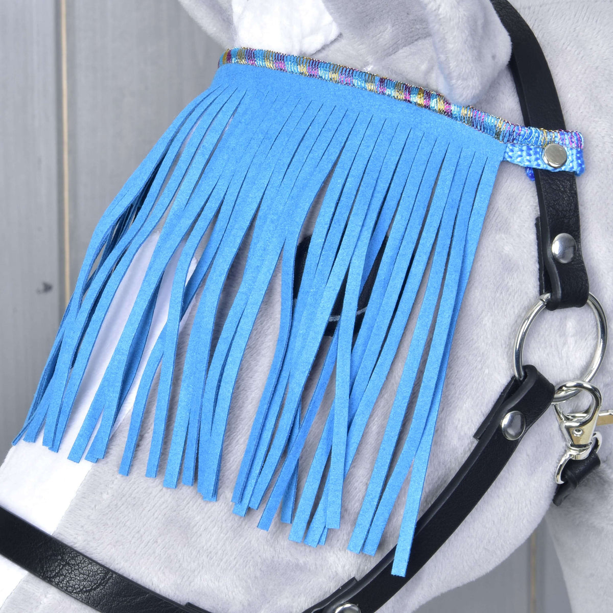 Gros plan sur les franges bleues suspendues à un galon arc-en-ciel brillant devant l’œil d’un Hobby Horse gris