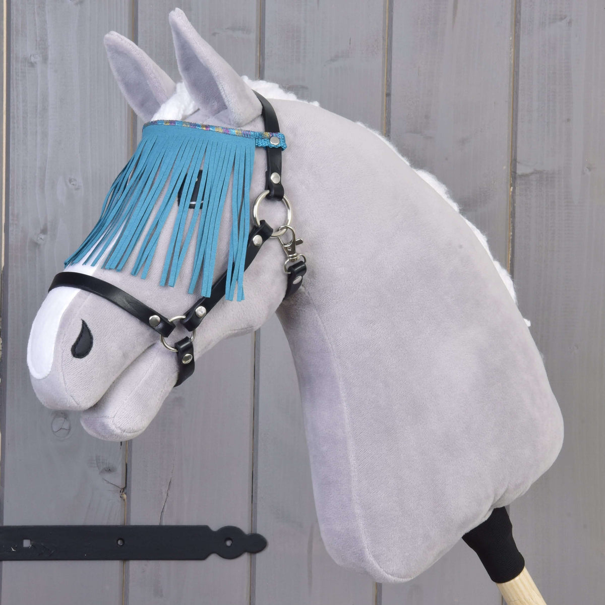 Hobby Horse gris en peluche à crinière blanche portant le licol noir, franges turquoise tombant sur les yeux