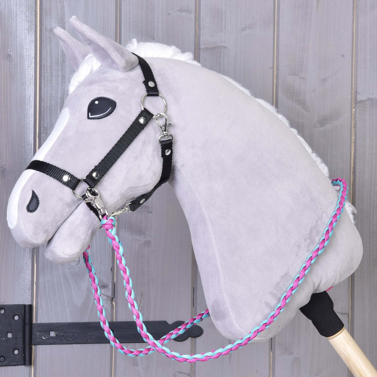 Hobby Horse en peluche gris avec licol noir et les rênes tricotées rose et bleu accrochées aux anneaux latéraux