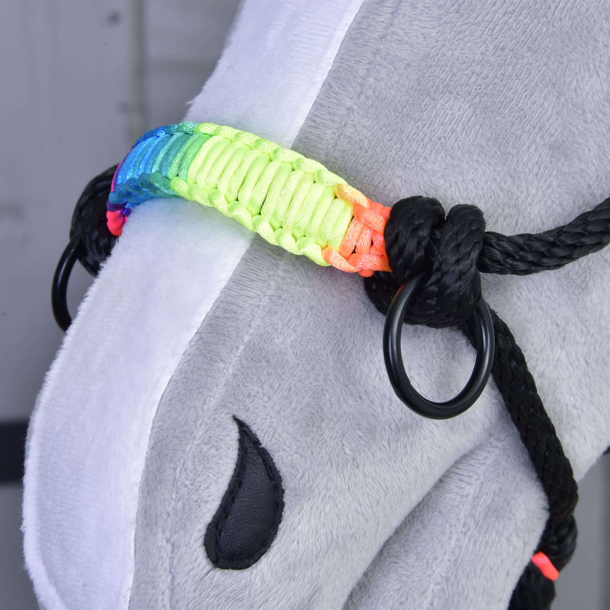 Close-up of the rope halter's rainbow braided noseband, black ring and knots on a grey plush Hobby Horse