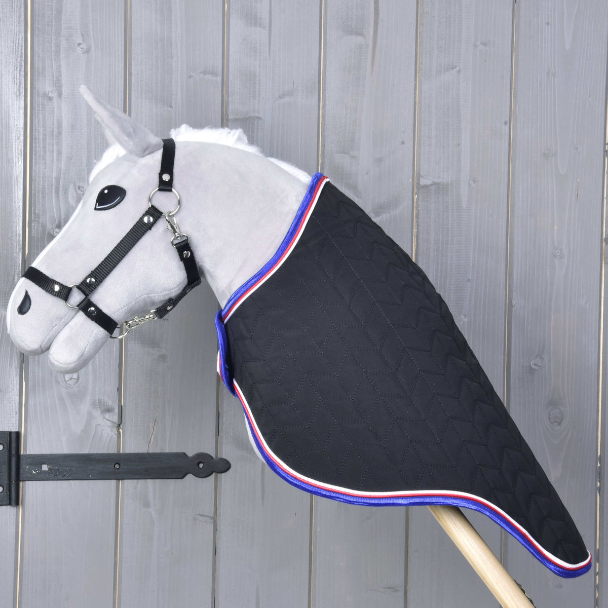 Hobby Horse gris de profil dans la couverture de voyage matelassée noire qui couvre toute l’encolure jusqu’au bâton en bois