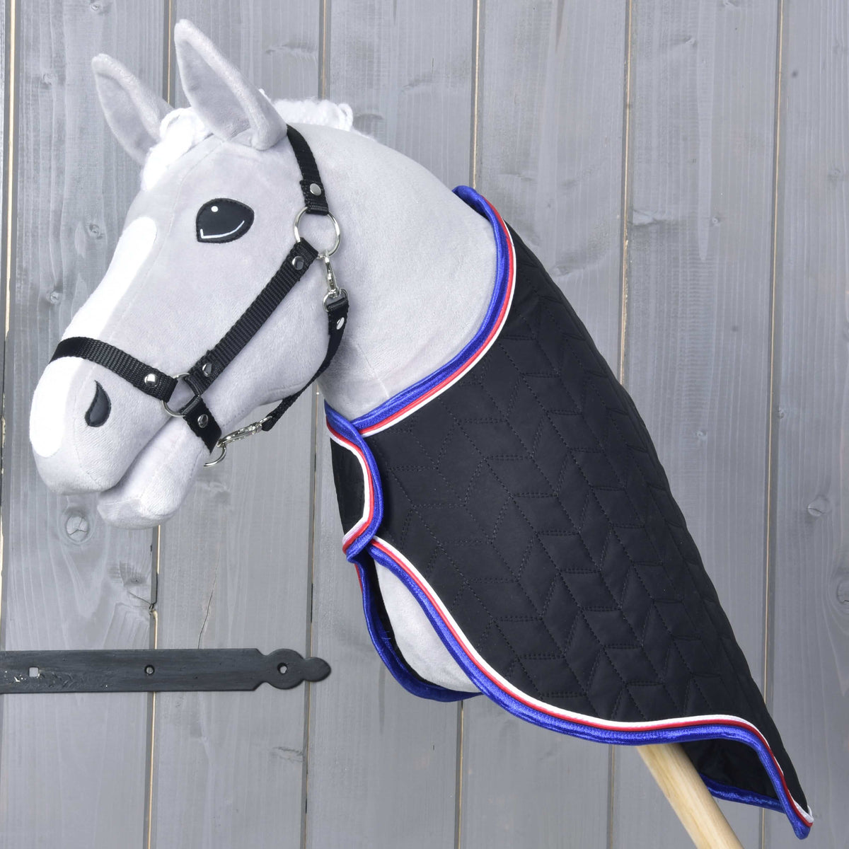 Hobby Horse gris avec licol noir portant la couverture de voyage matelassée noire bordée de bleu, rouge et blanc, vue de trois quarts