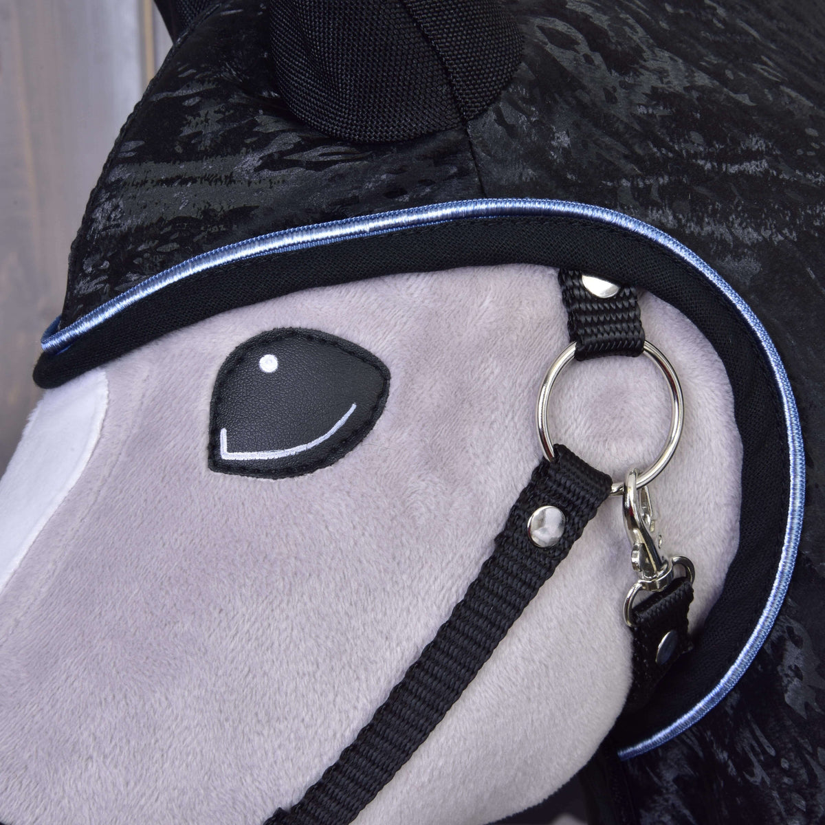 Gros plan sur le passepoil bleu clair autour de l’ouverture de tête de l’imperméable noir près du licol noir d’un Hobby Horse