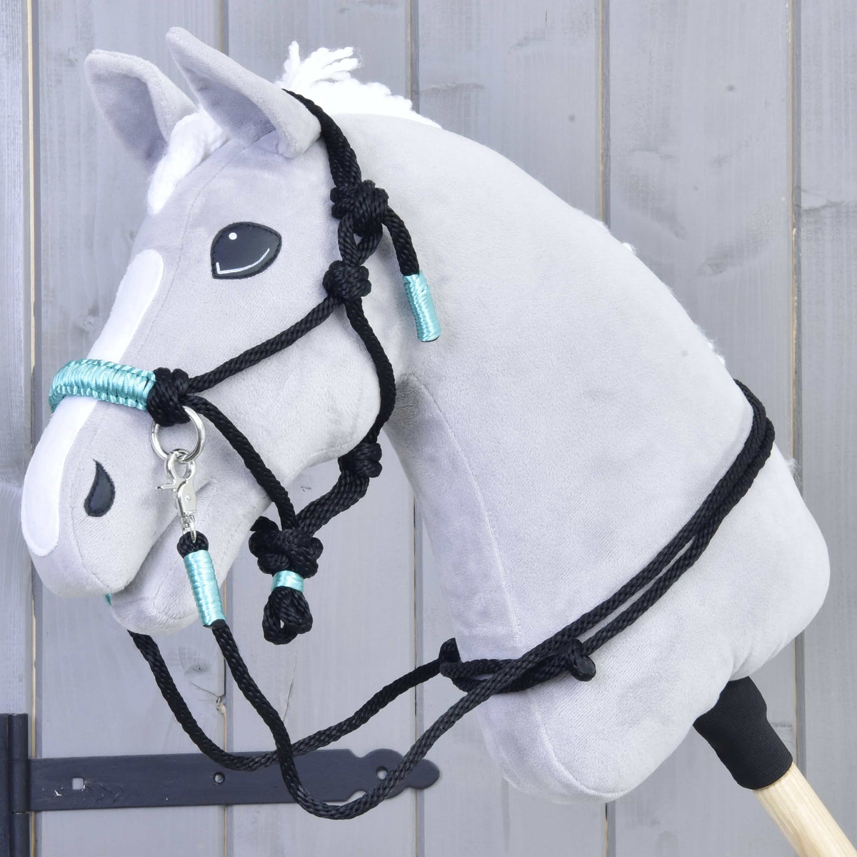 Hobby Horse gris portant le licol en corde noire à nœuds et enroulements turquoise, avec rênes noires assorties sur l’encolure