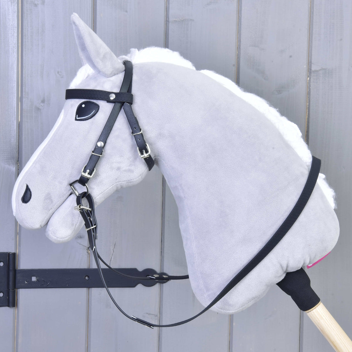 Hobby Horse gris de profil gauche portant la bride noire en similicuir, les rênes posées sur l’encolure