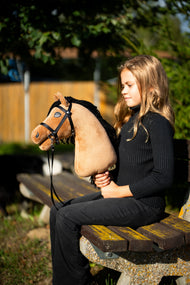 Meisje in zwarte trui op een bankje in de avondzon met Hobby Horse Samantha in een zwart hoofdstel met teugels
