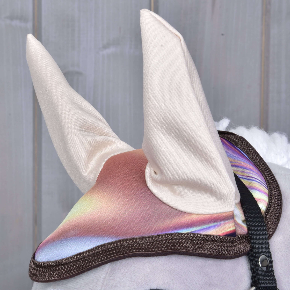 Gros plan sur le bonnet d’oreilles aux hautes oreilles crème, dessus rose et lilas chatoyant bordé de marron, sur un Hobby Horse gris