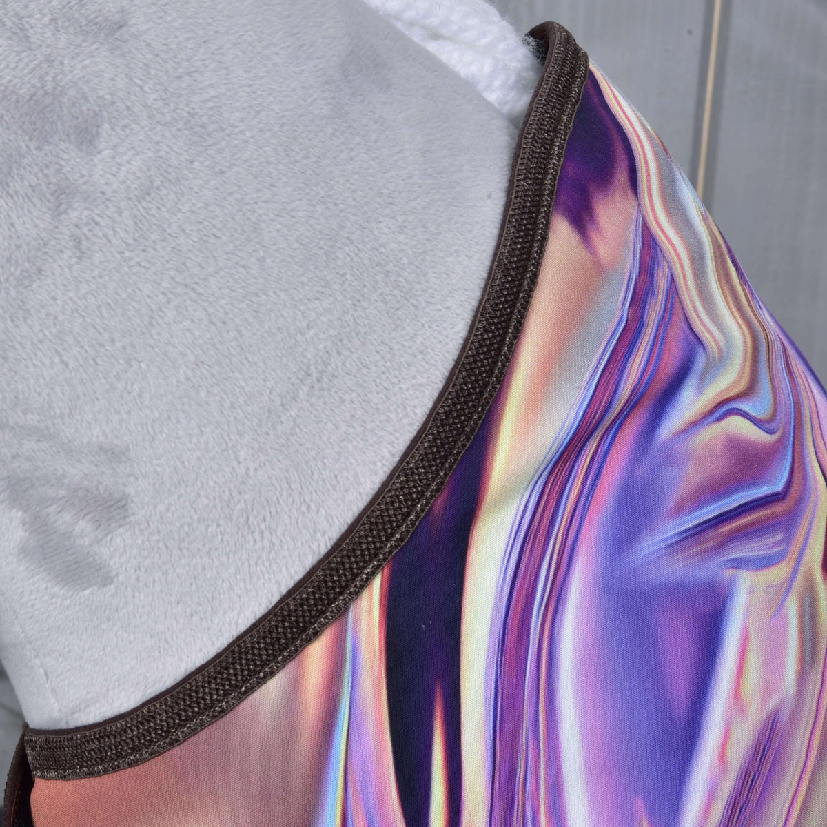 Gros plan sur le tissu irisé violet et rose de la couverture, bordé de marron le long de l’encolure d’un Hobby Horse gris