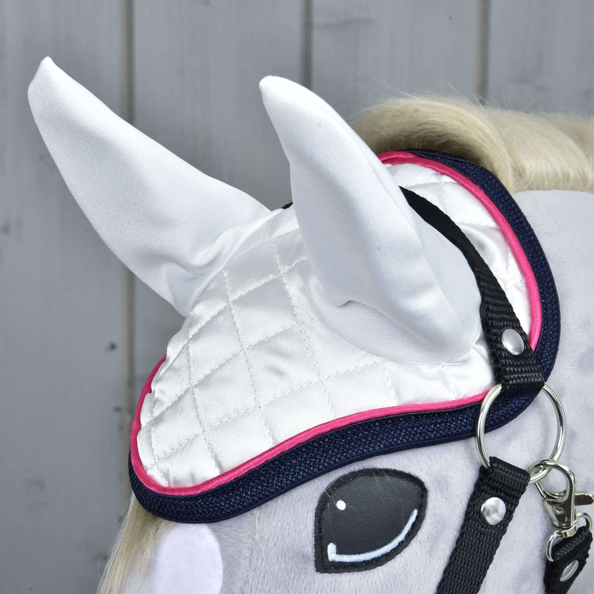 Close-up of the white quilted satin ear bonnet with white ear covers, pink piping and navy binding on a grey plush head