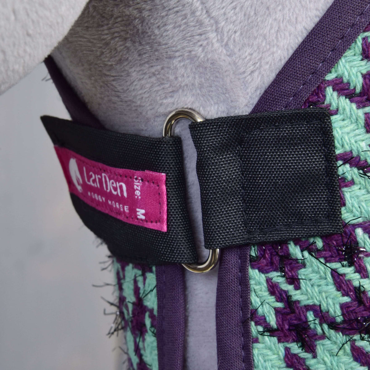 Borstsluiting van de deken uit Set Harmony Green: zwarte riem, metalen ring, roze LarDen-label en paarse bies