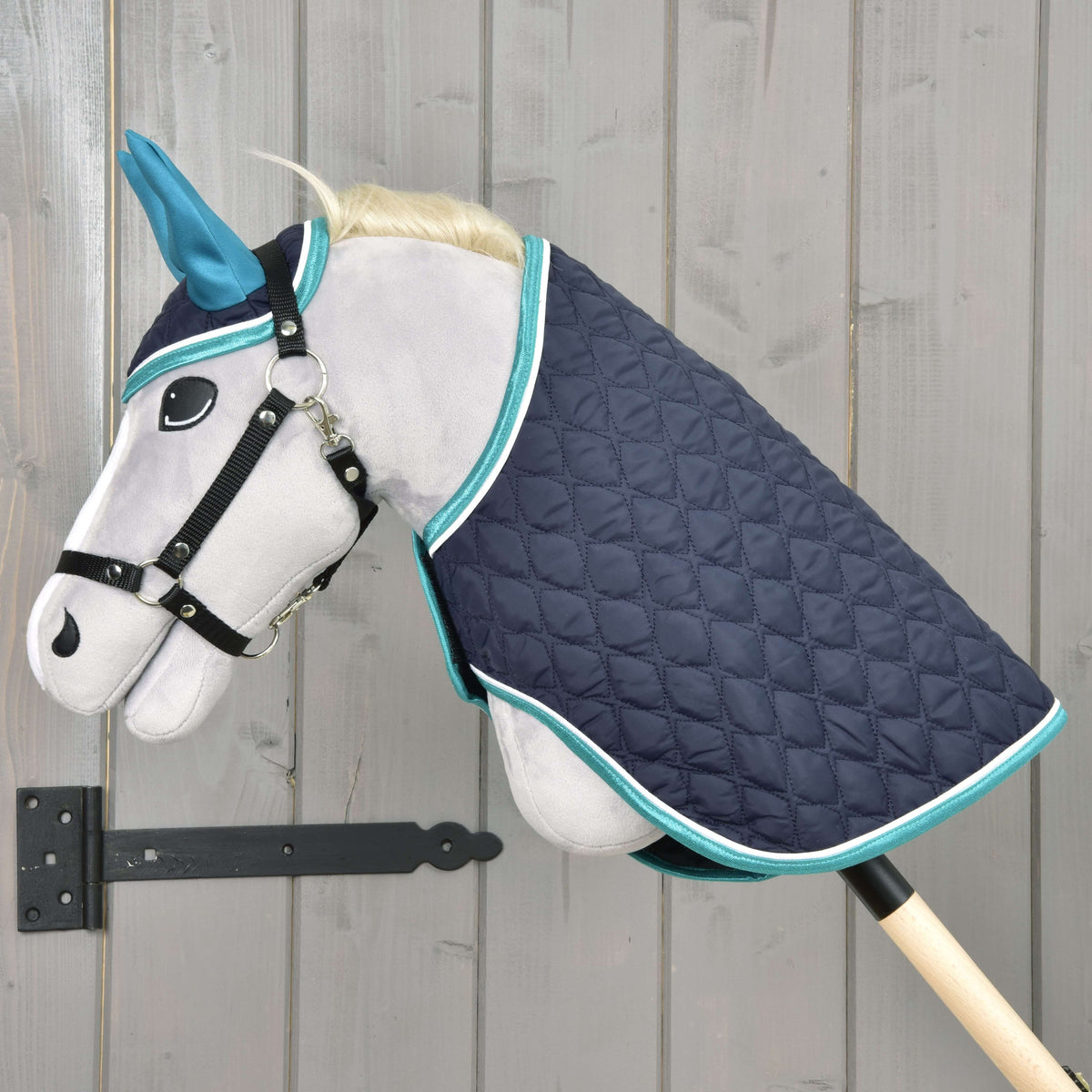 Light grey Hobby Horse in a black halter wearing the Set Supreme Turquoise, a navy quilted blanket with turquoise trim