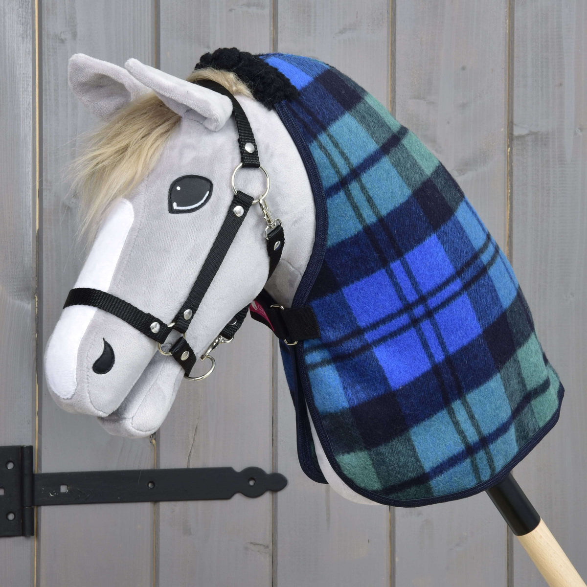 Grijze pluche Hobby Horse met zwarte halster in de blauw-groen geruite staldeken voor een grijze houten wand