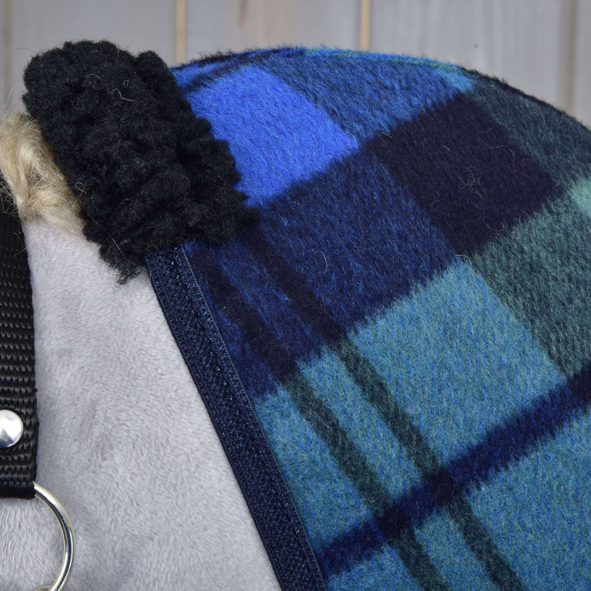 Close-up van de zwarte krullende fleece bij de schoft en de marineblauwe bies op de blauw-groen geruite fleece