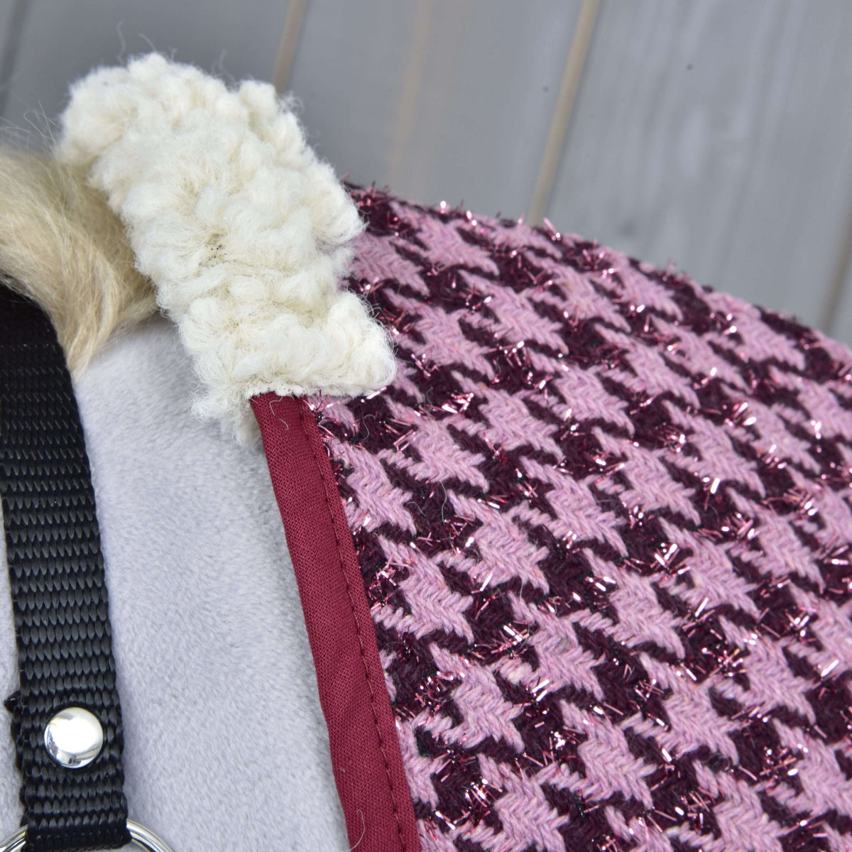 Close-up van de crème fleece bij de schoft, de bordeauxrode bies en het glinsterende roze pied-de-poule weefsel