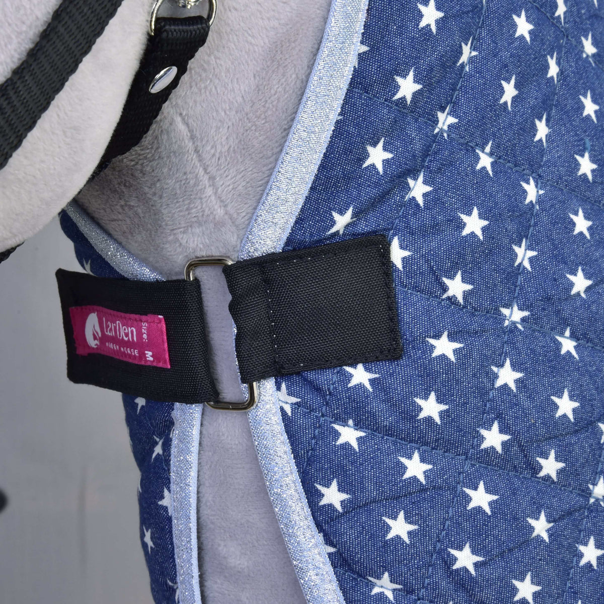 Gros plan sur la sangle de poitrail noire à boucle métallique et étiquette LarDen rose de la couverture d’écurie Star marine pour Hobby Horse