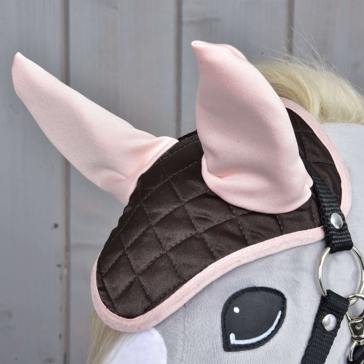 Gros plan sur le bonnet d’oreilles Chocolate porté par un Hobby Horse gris, oreilles rose clair au-dessus du satin brun matelassé