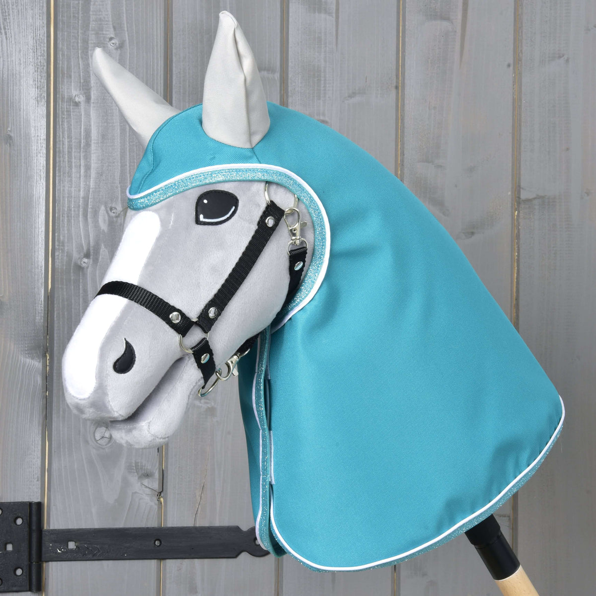 Hobby Horse gris avec licol noir portant l’imperméable turquoise à capuche et oreilles gris clair, qui couvre la tête et l’encolure