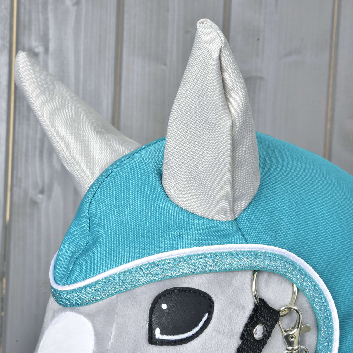 Gros plan sur la capuche de l’imperméable turquoise sur un Hobby Horse gris : oreilles gris clair et bordure pailletée à passepoil blanc