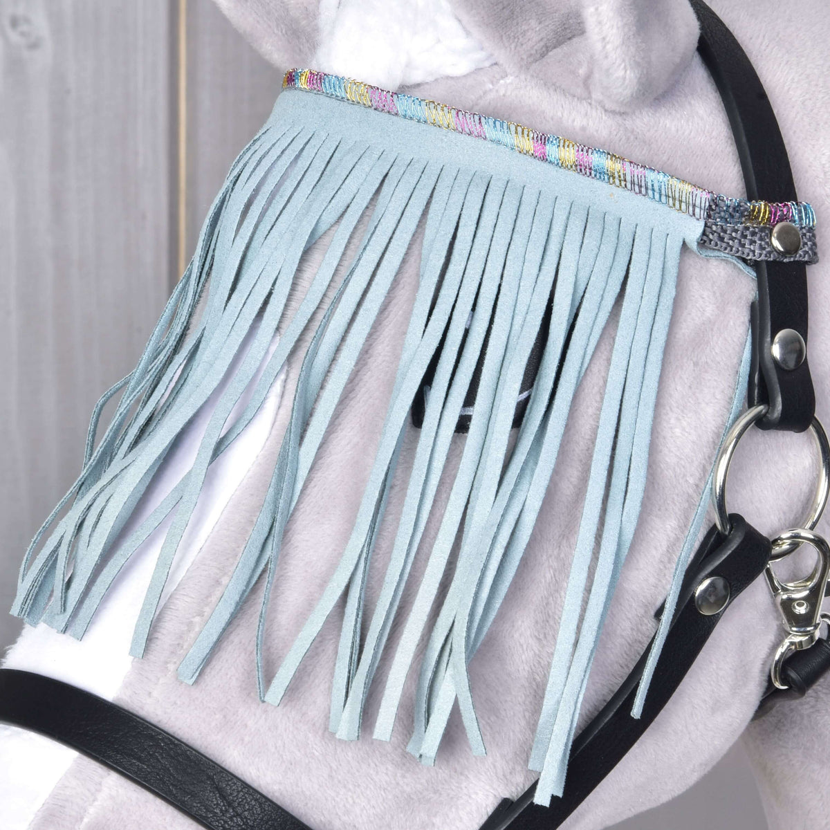 Gros plan sur les franges turquoise pâle et le galon arc-en-ciel pastel près du mousqueton argenté sur un Hobby Horse gris