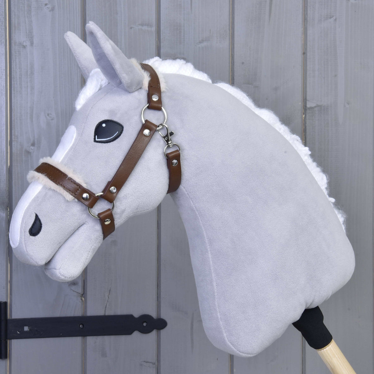 Lichtgrijze Hobby Horse met witte manen in het bruine halster van kunstleer met crèmekleurig bont op neusriem en kopstuk