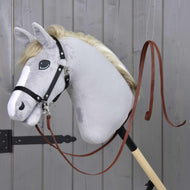 Lichtgrijze Hobby Horse met zwarte halster en de open westernteugels donkerbruin eraan vastgeklikt, voor een grijze houten deur