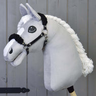 Grijze pluche Hobby Horse met gevlochten witte manen en de zwarte halster met zwart bont voor een grijze houten wand