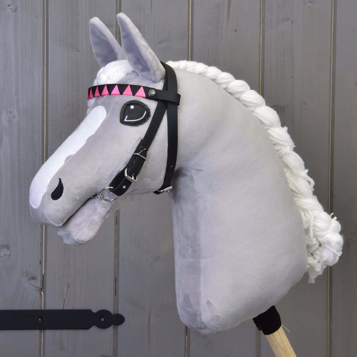Grijze pluche Hobby Horse met gevlochten witte manen en het zwarte hoofdstel met hoofdband in roze en zwarte driehoeken