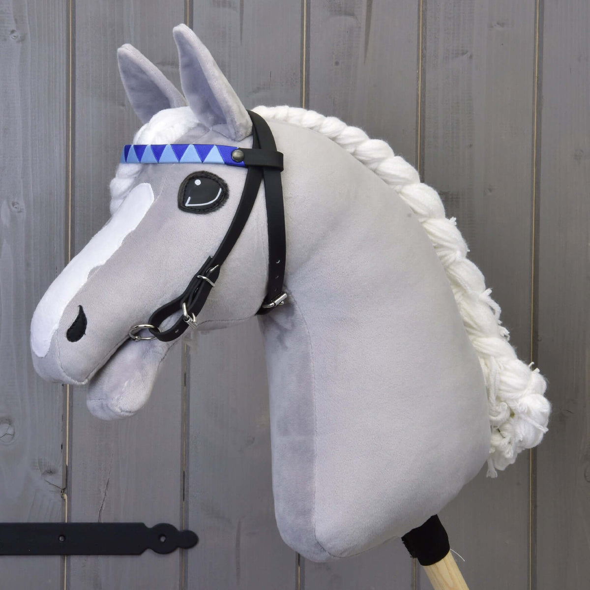 Grijze pluche Hobby Horse met gevlochten witte manen en het zwarte hoofdstel met hoofdband in blauwe driehoeken