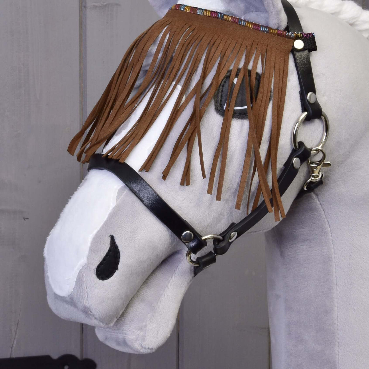 Close-up van de bruine franjes van kunstsuède met kleurrijke geweven rand aan de zwarte halster van een grijze Hobby Horse