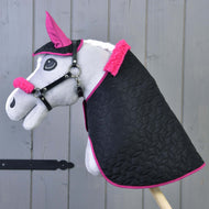 Grijze pluche Hobby Horse met zwarte gewatteerde deken, oornetje en halster met fuchsia bont voor een houten wand
