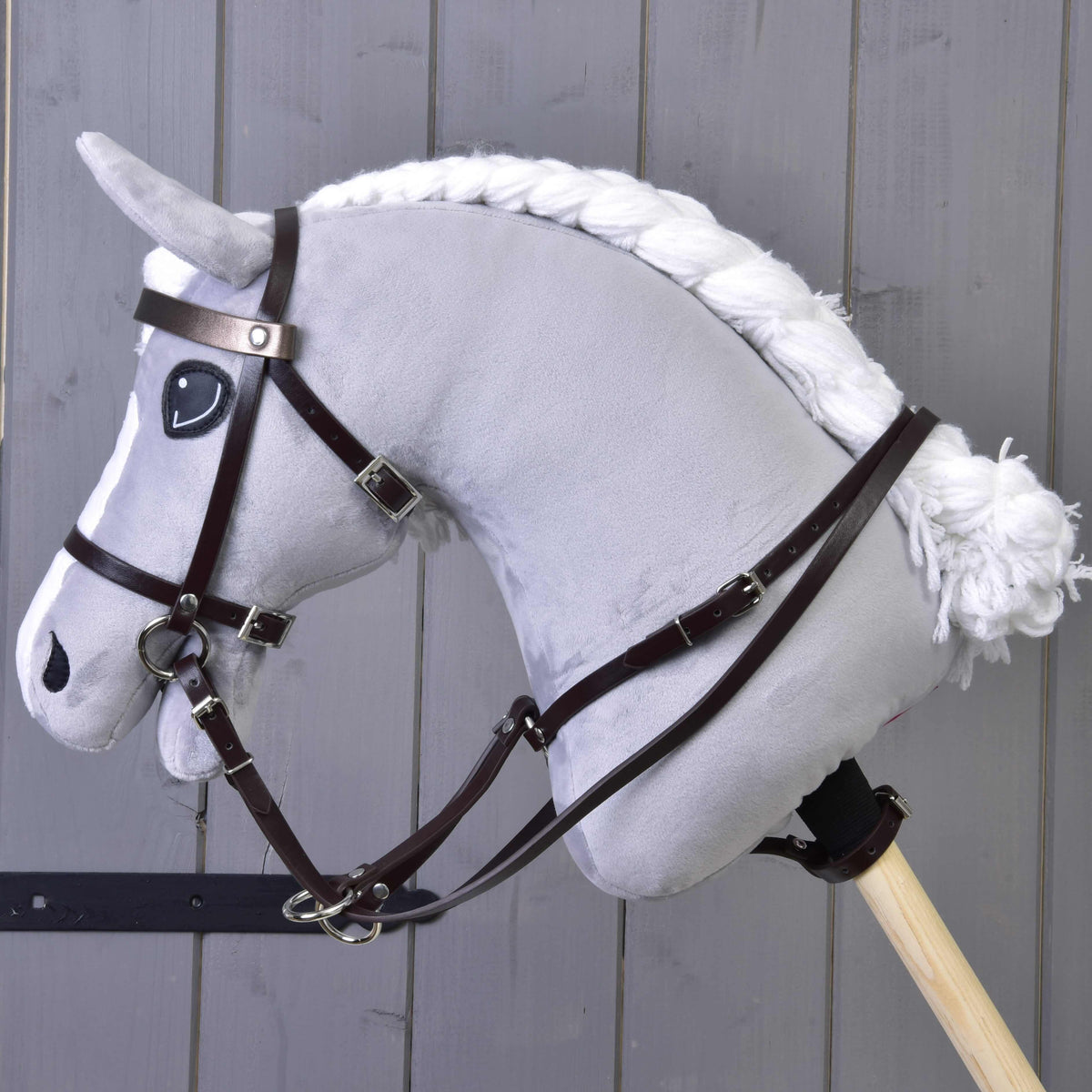 Grijze pluche Hobby Horse met gevlochten witte manen, donkerbruin hoofdstel, teugels en de bruine martingaal