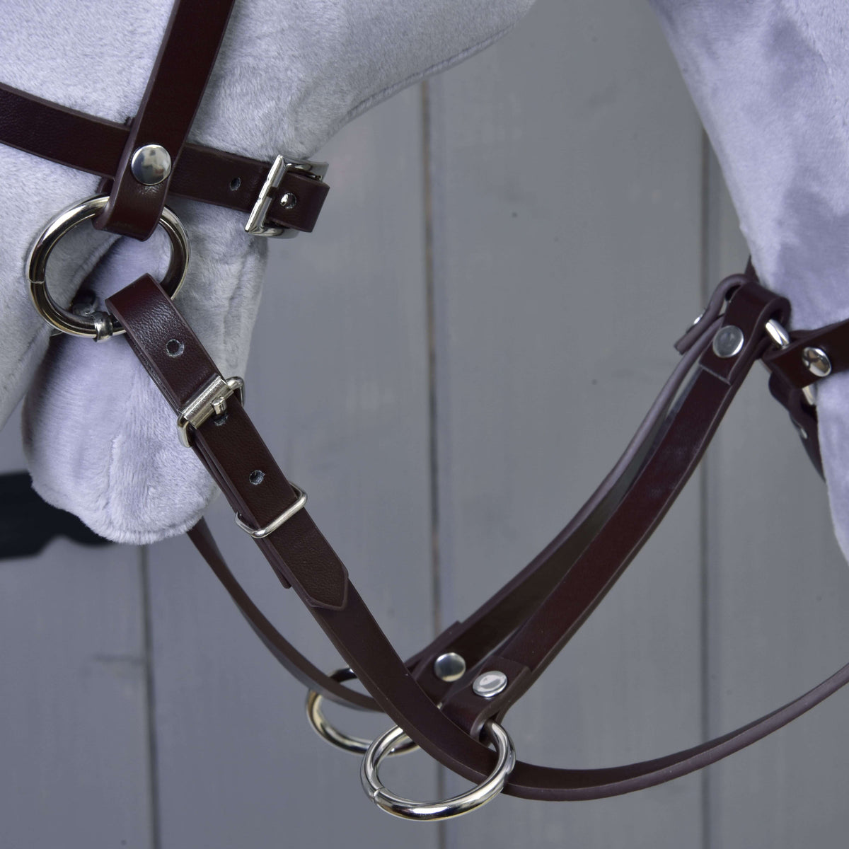 Close-up van de donkerbruine kunstleren martingaal met zilverkleurige ringen en de teugels op een grijze Hobby Horse