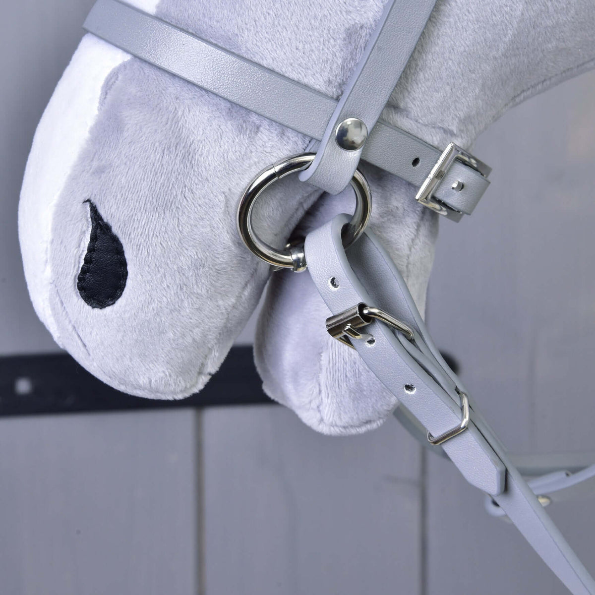 Close-up of the grey leatherette noseband with a silver ring and the buckled rein on a grey plush Hobby Horse