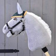 Grey plush Hobby Horse with a black halter wearing the green quilted ear bonnet with mustard trim, wooden wall